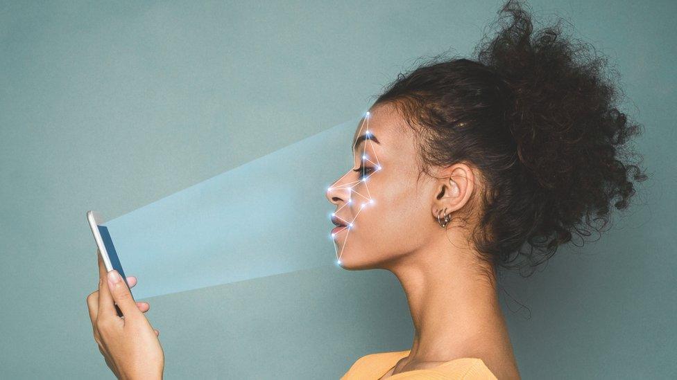 A woman holds up her phone in front of her as it scans her face with points of light in this photo illustration combination