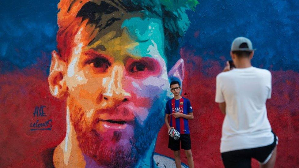 A boy sporting a Barcelona jersey poses for a photo beside a graffiti portraying Barcelona's Argentinian forward Lionel Messi on June 17, 2017 in Barcelona