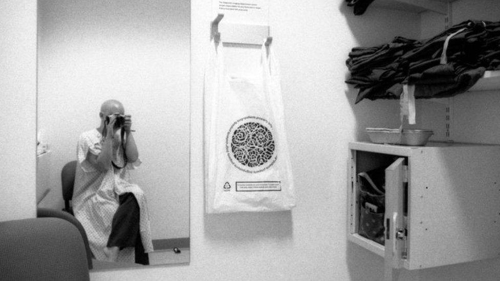 A woman taking a photo of herself in a hospital gown in the mirror