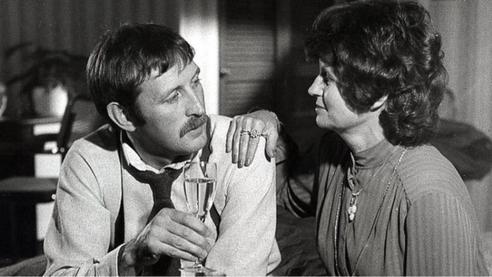 Dafydd Hywel in black and white holding a beer alongside a woman