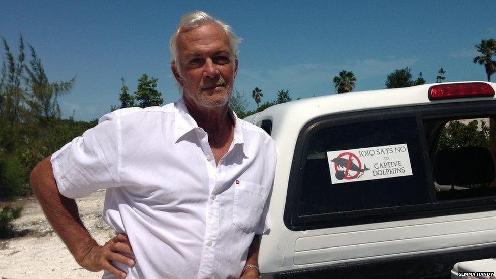 Tim Ainley stands next to his car with a bumper sticker reading "Jojo says no to captive dolphins".