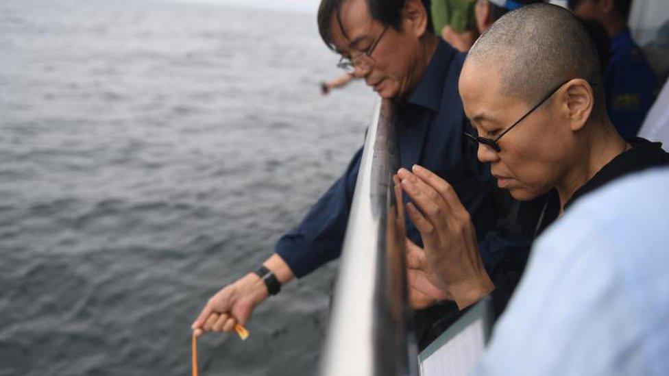 Liu Xiaobo's wife Liu Xia (R) prays as his ashes are scattered in the sea near Dalian