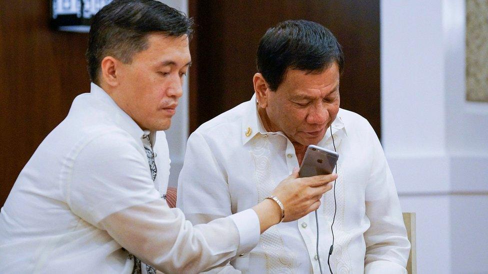 Filipino President Rodrigo Duterte (R), assisted by Special Assistant to the President Christopher Lawrence Go (L), speaking to US President Donald J. Trump during a phone call on the sidelines of the gala dinner