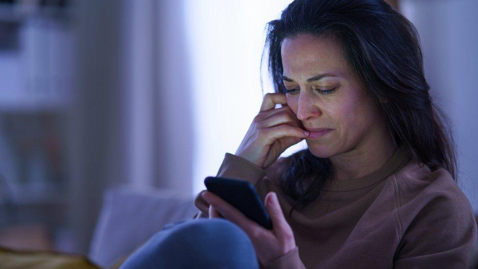 A woman looks upset while looking at her mobile phone