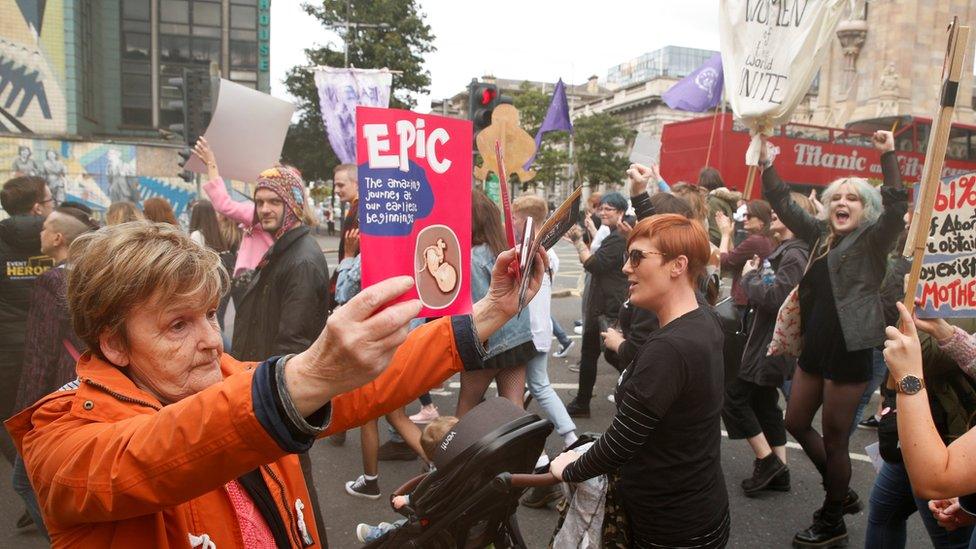 An anti-abortion supporter holds up leaflets as pro-choice demonstrators march in Belfast