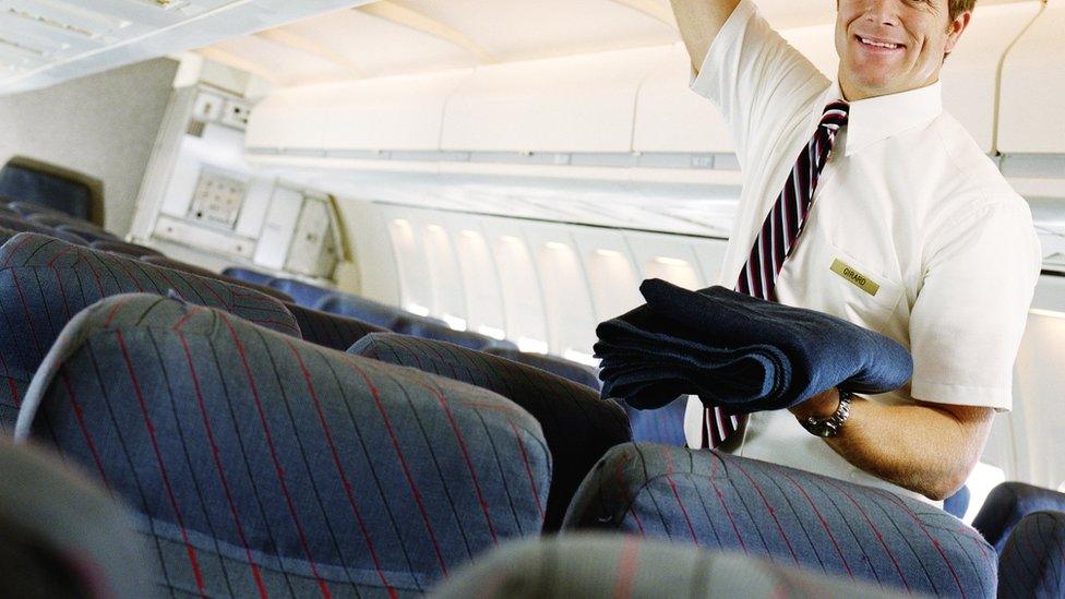 A stock image of a male flight attendant putting a blanket in overhead locker