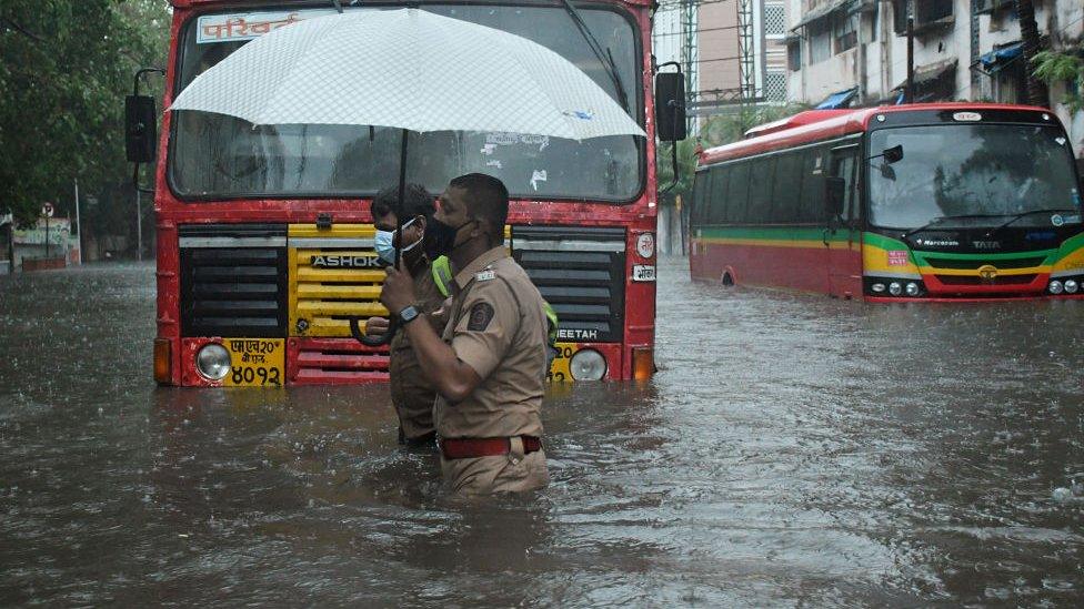 A policeman helps a public transport driver to cross a flooded street due to heavy rain caused by cyclone 'Tauktae' in Mumbai.