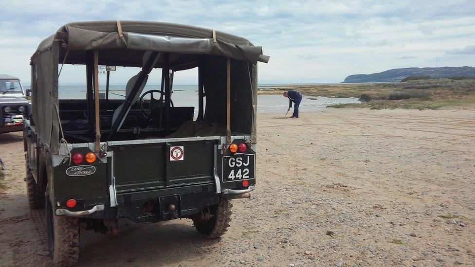 Jamie sketches in the sand next to Land Rover vehicle