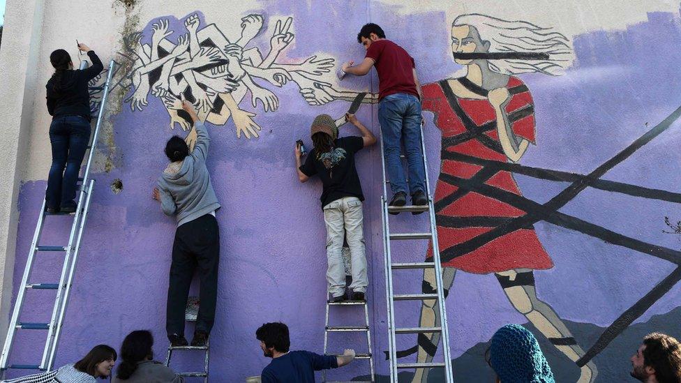 Youths work on a mural against violence toward women in Ankara