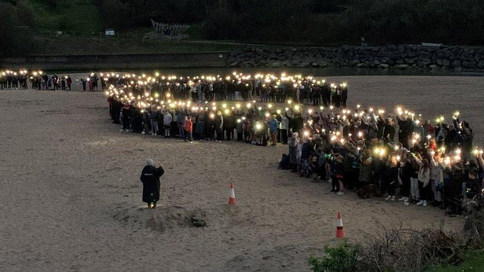 Y gymuned yn chwifio golau gyda'u ffonau symudol ar y traeth