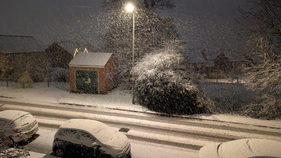 Snow covered road with cars parked and snow falling