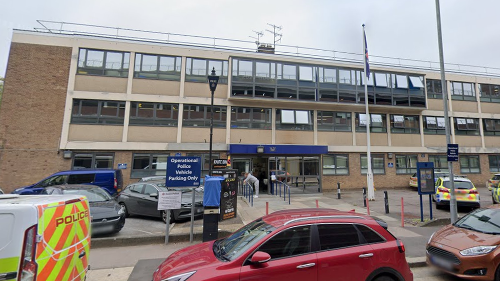 The exterior of Basildon police station. A modern, three-storey brick building with cars parked outside.