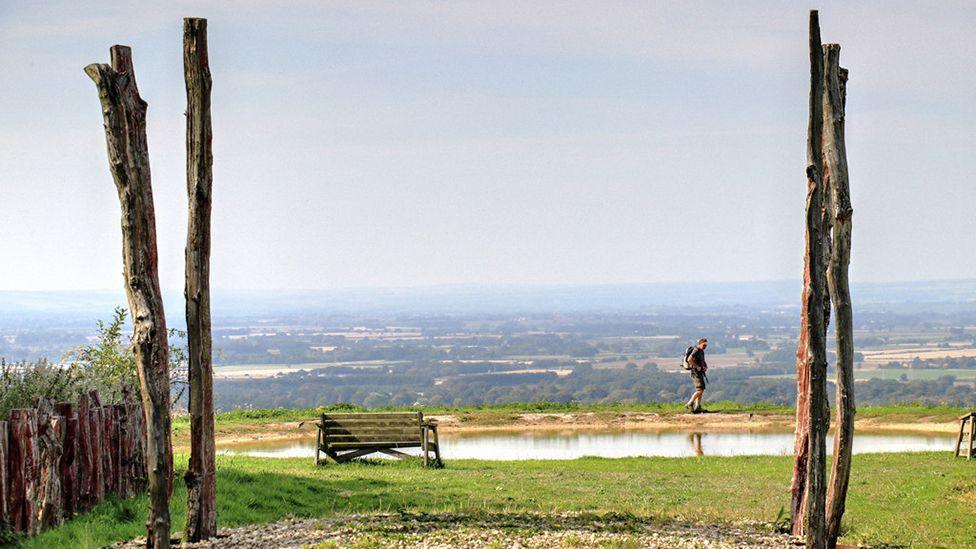 A sculpture of tree trunks frames a walker with a view of the Yorkshire Wolds stretching away in the distance
