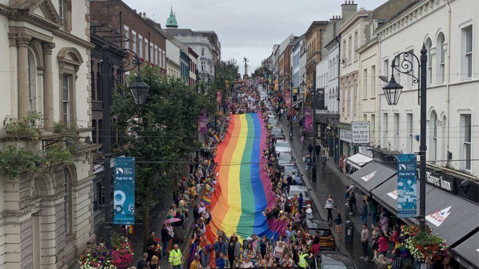 A huge crowd, holding aloft a rainbow flag, walk down Derry's Shipquay street, as others line both sides of the street to allow the parade to pass