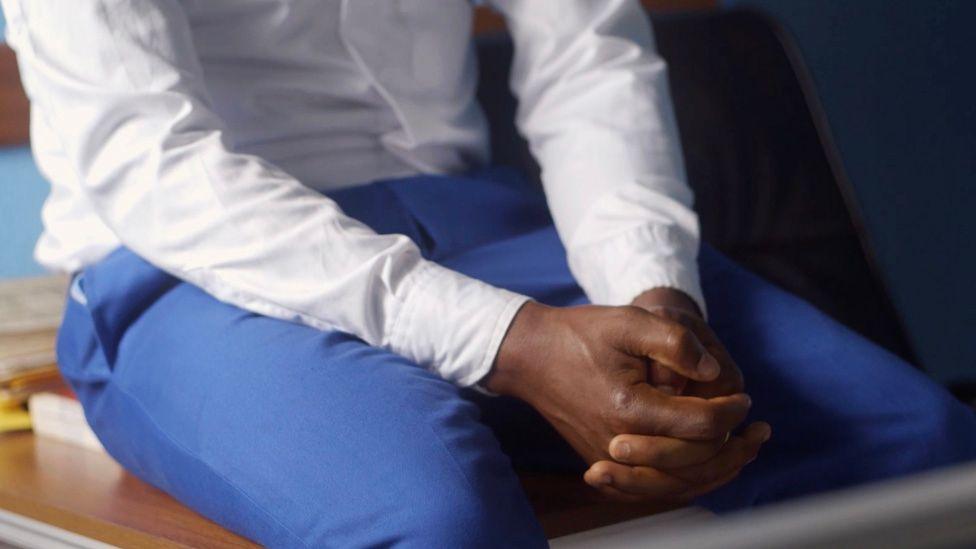 A photo of John's hands clasped in his lap. You can't see his face