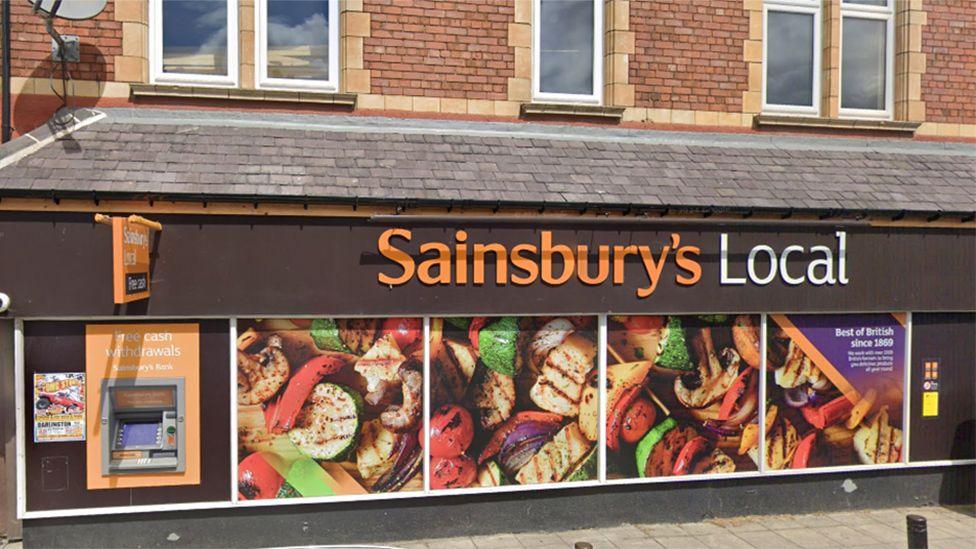 A Sainsbury's Local branch on Corporation Road in Darlington, with the name written in orange and white letters above pictures of chicken and vegetable kebabs covering what would be the windows.