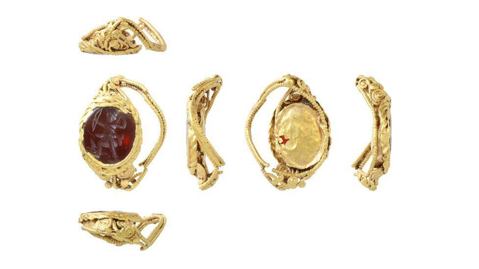 Six views of a gold Roman ring. Its front on the left reveals a red stone carved with a view of Diana pulling back her bow surrounded by its gold setting. The other views show how crumpled it has become over the centuries