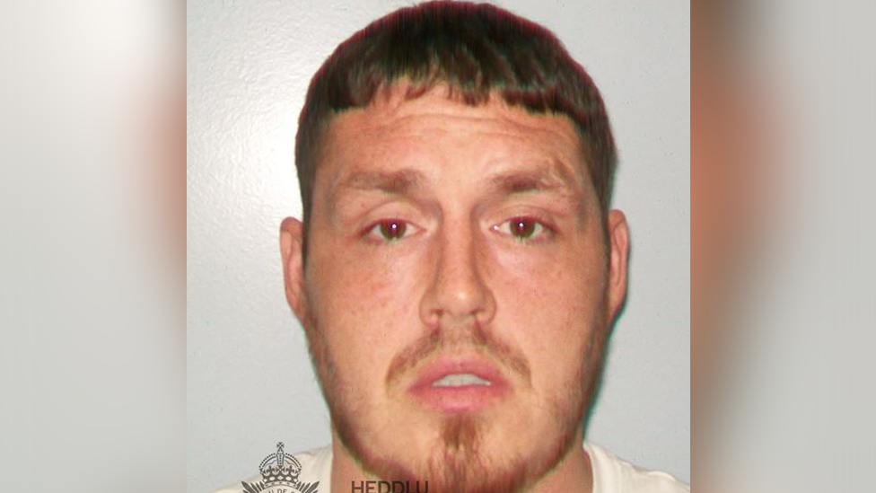 A police custody photo of Johnathan. he has short cropped brown hair and a thin reddish beard