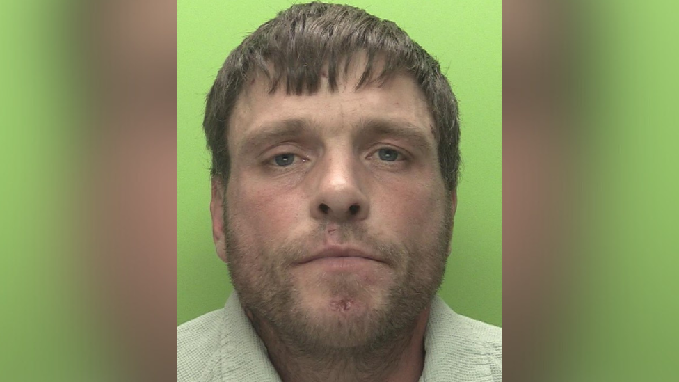 A mugshot of Gediminas Cepla, a white man wearing a cream corduroy shirt. He has straight, short brown hair and a very short, scruffy-looking beard. He is expressionless.