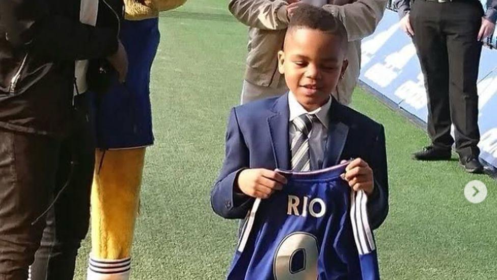 Photo of Rio Ngumoha as an eight-year-old boy holding a Chelsea shirt.