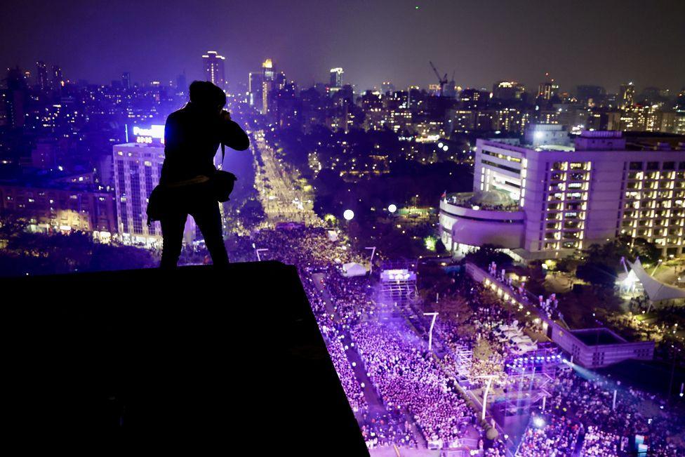 A person takes photos of crowds attending New Year's Eve celebrations prior to the Taipei 101 firework display, in Taipei, Taiwan, 31 December 2024.