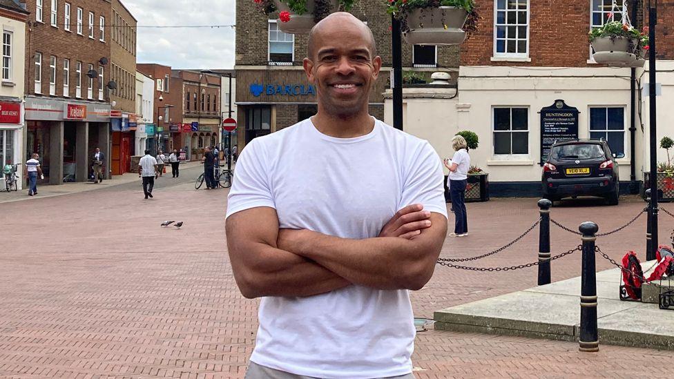 Ben Obese-Jecty wearing a white t-shirt with war memorial and shops in the background