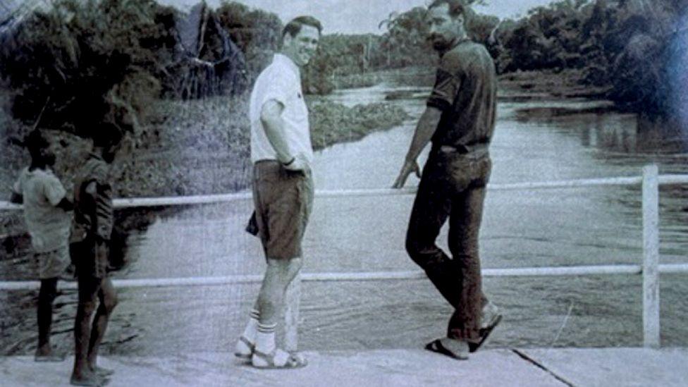 A black and white photo of two men and some children standing on a bridge