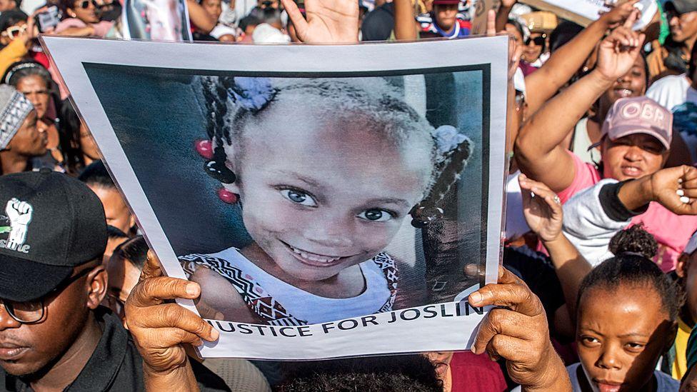 Someone in a crowd holds up a poster of Joshlin Smith with the words underneath her image saying, 'Justice for Joslin (sic)'.
