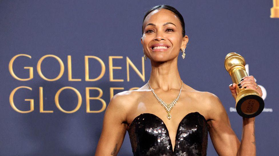 Zoe Saldaña holding up a Golden Globe trophy