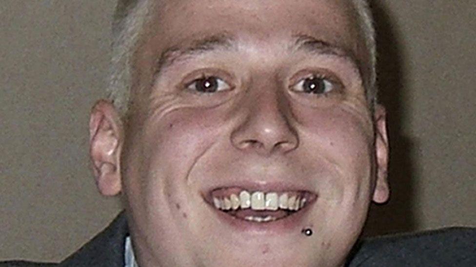 A close-up of Phil Beer who has short blonde hair and his chin raised and is smiling broadly. He has a stud under his lip on the left. His grey jacket can just be seen.