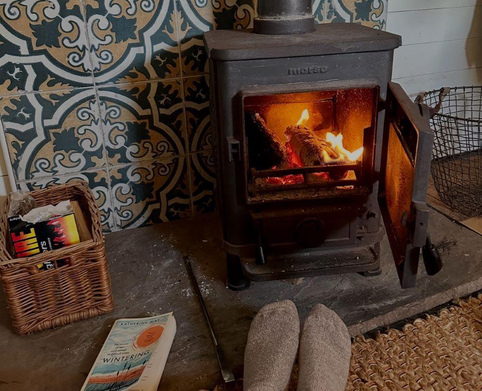 A log-burning fireplace, a book and feet in front of decorative blue and yellow tiles