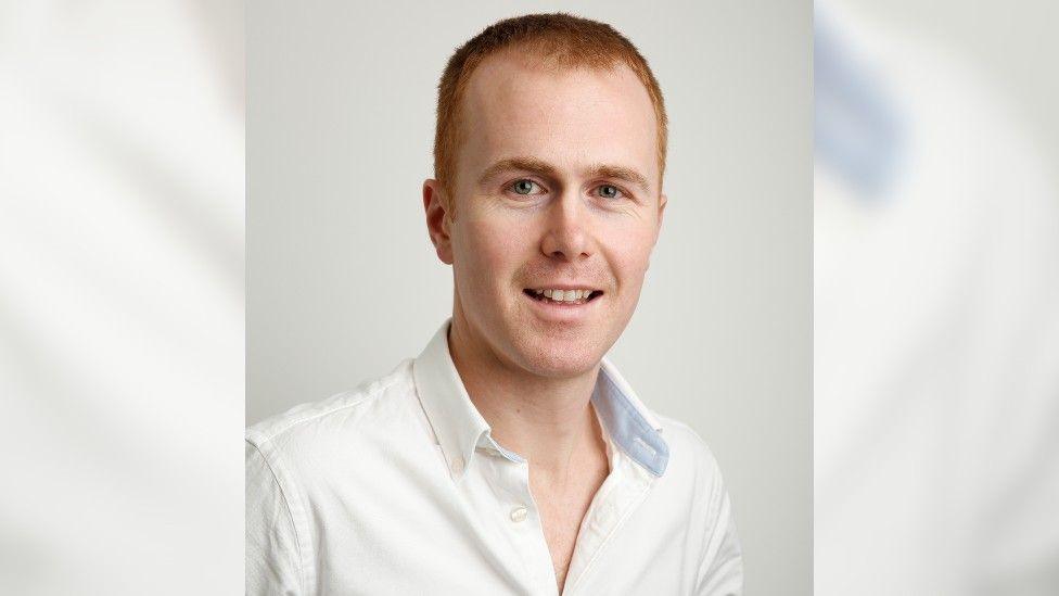 Close up of Mr Freeman who has red hair and blue eyes. He is wearing a white shirt and stood in front of a white background.