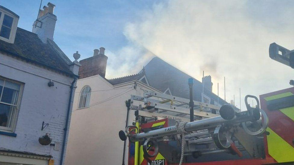 Back of fire engine with cream building in background with smoke coming from the roof