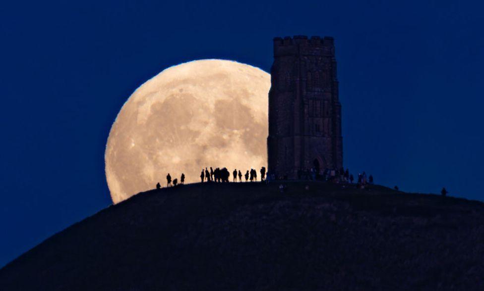 People gather as a full harvest supermoon rises behind Glastonbury Tor on September 17, 2024 in Glastonbury, England.