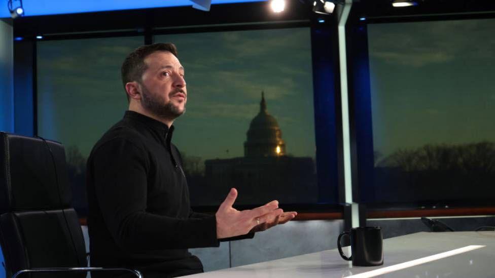 Zelensky gestures with his hands as he sits behind a desk