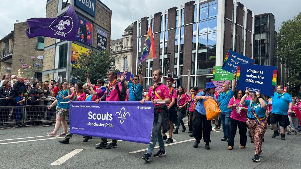 Members of the Scout Association, wearing pink and blue T-shirts and carrying purple flags and banners, take part in the Manchester Pride parade