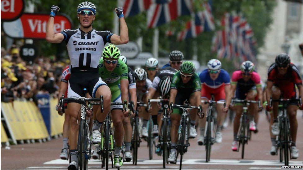 Marcel Kittel in black and white raising his fists in triumph as he heads a pack of riders to win the third leg of the Tour de France, 2014