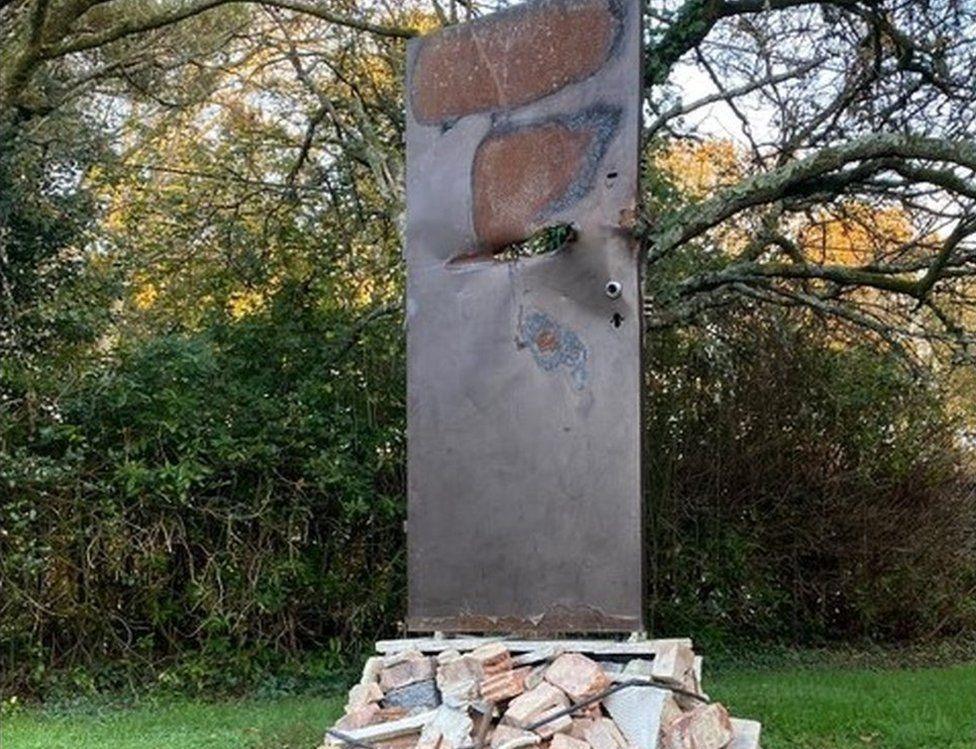 Pile of rubble with silver-coloured door standing on top - it has a hole through it and large burn marks across the top.