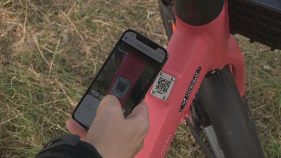 A man wearing dark clothing holding a phone which is scanning a QR code on a red bike frame.