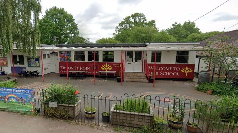 The entrance to Tipton St John Primary School, a white and red building with a sign saying 'welcome to our school'