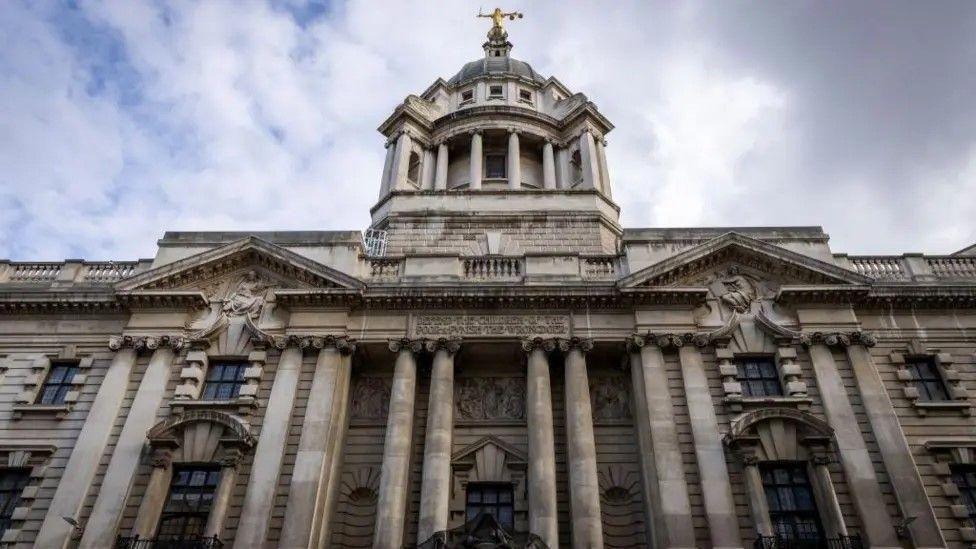 Old Bailey court. Classical-style pillars stand at the front of the pale stone building with a raised dome at the centre topped with a gold-coloured statue holding the scales of justice