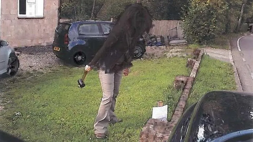 A West Berkshire Council officer standing in Maria Dobson's garden, with a mallet in her hand, standing next to a notice she hammered a post with the notice into her garden