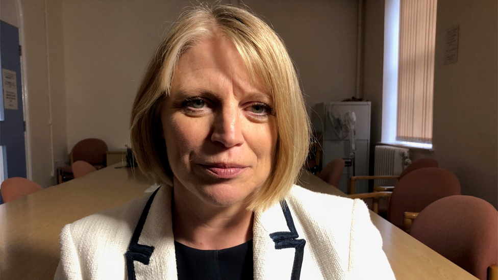 A woman with short blonde hair and white blazer looking into the camera