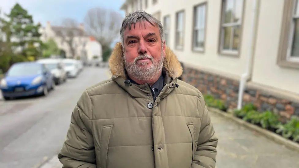 A bearded man with a light coloured anorak with a furry trim.