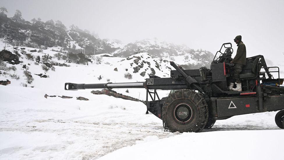 An Indian army soldier sits on a mobile artilery unit in the snow in the Himalayan mountains.  