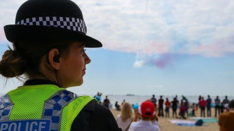 A female Dorset police officer watches crowds on a beach