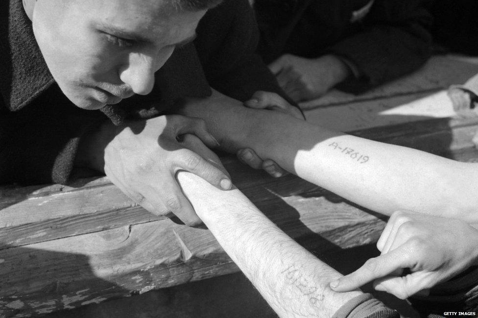 A young man checks the numbers tattooed on the arms of Jewish Polish prisoners coming from Auschwitz, in Dachau concentration camp after its liberation by the US army at the end of April 1945