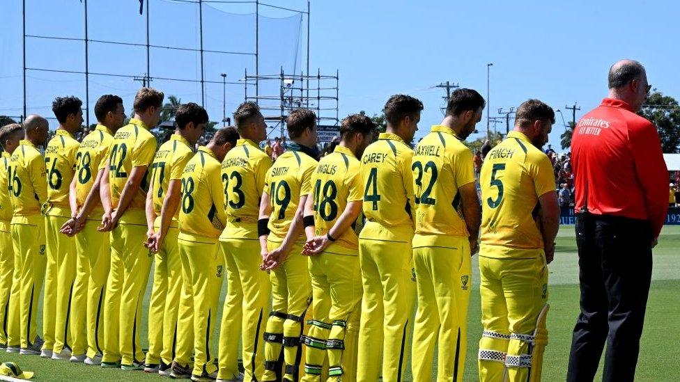 Cricket players in yellow kit stand in silence.