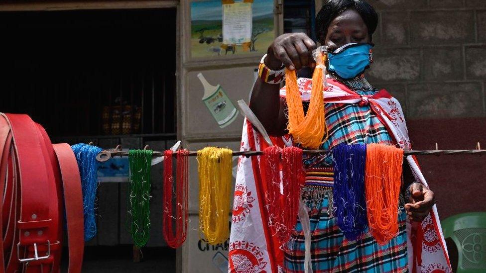 A woman sets up her stand displaying handmade beaded jewellery and leather belts in Talek in the Maasai Mara, Kenya - June 2020