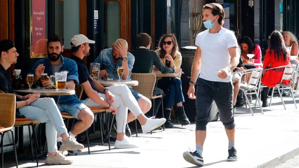 Man walking past people drinking outside a bar